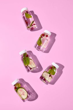 Boş pembe arka planda plastik şişe modeli. Salatalık, nane ve böğürtlenli detoks suyundan yapılmış. Şişe maketi tasarla. Sağlıklı, spor ya da diyet için içecek. Şeffaf şişede detoks içeceği