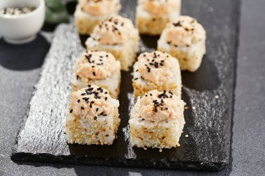 Karanlık taş masada Maki suşisi. Deniz kabuğu ve yengeçli suşi rulosu. Siyah arkaplan, yapraklar ve sert gölgeli japon tarzı menü