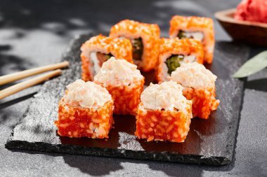 Karanlık taş masada Maki suşisi. Tobiko ile Kaliforniya maki 'si. Somonlu suşi, içinde salatalık, dışarıda maguro, yengeç. Siyah arka planı, yaprakları ve sert gölgesi olan Japon tarzı bir menü.