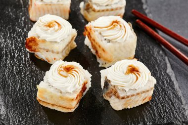 Kara tahtada Maki suşisi. Yılanbalıklı Unagi maki. Yılanbalığı, krem peynir ve unagi soslu suşi. Siyah arka planı, yaprakları ve sert gölgesi olan Japon tarzı bir menü.