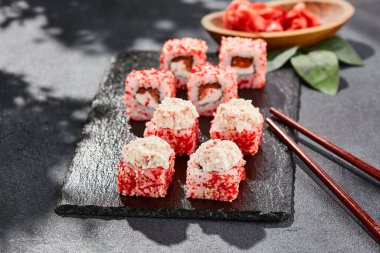 Kara tahtada Maki suşisi. Yengeçli Maki dürümü. Yengeç, krem peynir ve tobika ile suşi rulosu. Siyah arka planı, yaprakları ve sert gölgesi olan Japon tarzı bir menü.