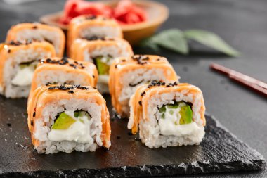Kara tahtada Maki suşisi. Fırında somonlu sıcak Philadelphia maki. Izgara somon, krem peynir ve avokado ile suşi rulosu. Siyah arka planı, yaprakları ve sert gölgesi olan Japon tarzı bir menü.