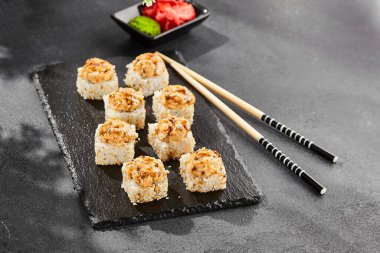 Kara tahtada fırında Maki suşisi. Yılanbalıklı sıcak unagi maki. Fırında yılan balığı, peynir ve unagi soslu suşi rulosu. Siyah arka planı, yaprakları ve sert gölgesi olan Japon tarzı bir menü.