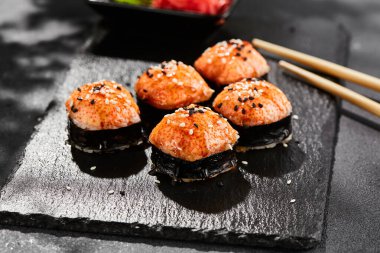 Kara tahtada fırında Maki suşisi. Sıcak unagi maki ve tobiko. Fırında peynirli suşi, masago ve unagi soslu. Siyah arka planı, yaprakları ve sert gölgesi olan Japon tarzı bir menü.