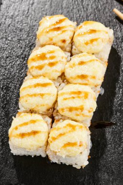 Kara tahtada fırında Maki suşisi. Unagi soslu sıcak peynirli maki. Üstünde fırında peynir ve unagi soslu suşi rulosu. Siyah arka planı, yaprakları ve sert gölgesi olan Japon tarzı bir menü.