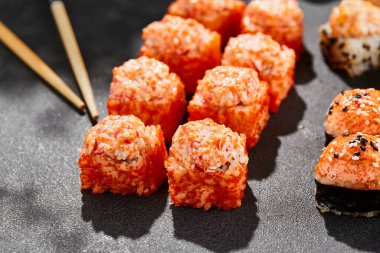 Ateşli maki, kara tahta üzerine kurulmuş. Fırında suşi ve sıcak ekmek. Somon, tobiko ve fırında peynirli suşi. Siyah arka planı, yaprakları ve sert gölgesi olan tarz konsept suşi menüsü