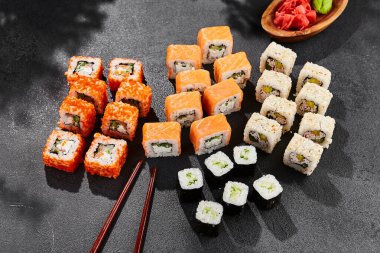 Maki suşisi karanlık tahtaya kurulmuş. Çeşitli ekmeklerle Maki seti. Suşi rulolarından - Philadelphia, California, hosomaki. Siyah arka planı, yaprakları ve sert gölgesi olan tarz konsept suşi menüsü