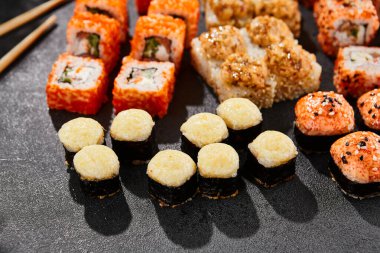 Maki suşisi koyu arkaplanda. Çeşitli ekmeklerle Maki seti. Suşi börekleri ve fırında maki karışımı. Siyah arka planı, yaprakları ve sert gölgesi olan tarz konsept suşi menüsü