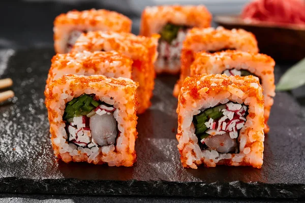 Maki sushi on dark stone table. California maki with tobiko. Sushi roll with crab,shrimp, cucumber inside, maguro outside. Style concept japanese menu with black background, leaves and hard shadow