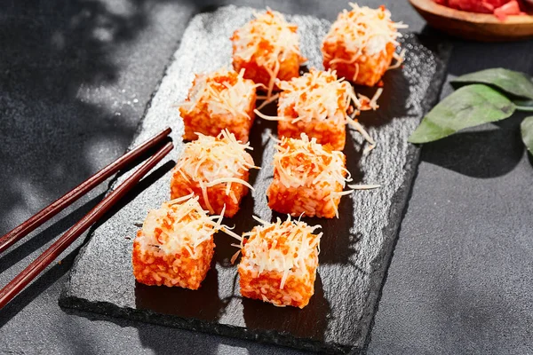 Karanlık taş masada Maki suşisi. Tobiko ile Kaliforniya maki 'si. İçinde balık olan suşi, dışında peynirli maguro. Siyah arka planı, yaprakları ve sert gölgesi olan Japon tarzı bir menü.