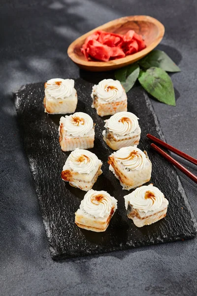 Kara tahtada Maki suşisi. Yılanbalıklı Unagi maki. Yılanbalığı, krem peynir ve unagi soslu suşi. Siyah arka planı, yaprakları ve sert gölgesi olan Japon tarzı bir menü.