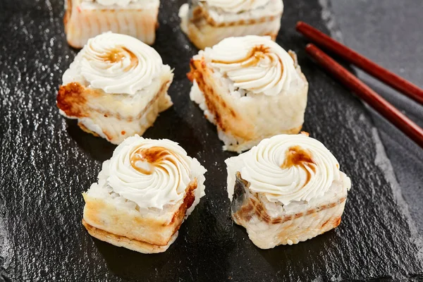 Kara tahtada Maki suşisi. Yılanbalıklı Unagi maki. Yılanbalığı, krem peynir ve unagi soslu suşi. Siyah arka planı, yaprakları ve sert gölgesi olan Japon tarzı bir menü.