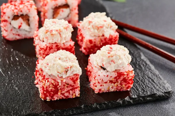 Kara tahtada Maki suşisi. Yengeçli Maki dürümü. Yengeç, krem peynir ve tobika ile suşi rulosu. Siyah arka planı, yaprakları ve sert gölgesi olan Japon tarzı bir menü.