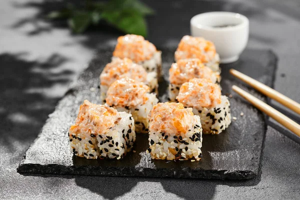 stock image Baked Maki sushi on dark slate. Hot sushi roll with salmon and cheese. Sushi roll sesame outside, baked salmon and cheese topped. Style concept japanese menu with black background, leaves and hard shadow