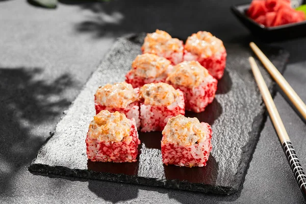 Kara tahtada fırında Maki suşisi. Somonlu sıcak suşi. Dışarıda tobiko ile suşi rulosu, fırında balık ve peynir. Siyah arka planı, yaprakları ve sert gölgesi olan Japon tarzı bir menü.