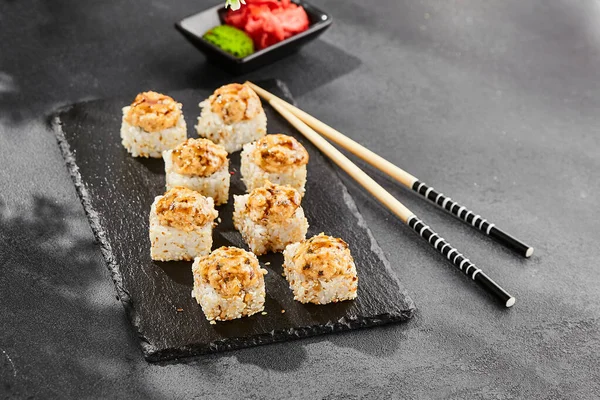 Kara tahtada fırında Maki suşisi. Yılanbalıklı sıcak unagi maki. Fırında yılan balığı, peynir ve unagi soslu suşi rulosu. Siyah arka planı, yaprakları ve sert gölgesi olan Japon tarzı bir menü.