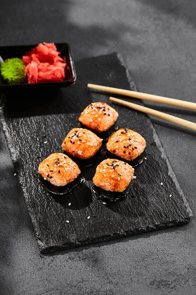Kara tahtada fırında Maki suşisi. Sıcak unagi maki ve tobiko. Fırında peynirli suşi, masago ve unagi soslu. Siyah arka planı, yaprakları ve sert gölgesi olan Japon tarzı bir menü.