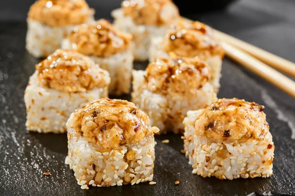 Kara tahtada fırında Maki suşisi. Yılanbalıklı sıcak unagi maki. Fırında yılan balığı, peynir ve unagi soslu suşi rulosu. Siyah arka planı, yaprakları ve sert gölgesi olan Japon tarzı bir menü.