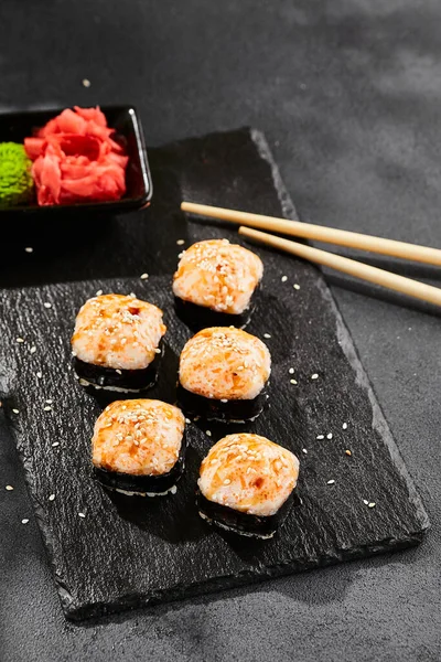 Kara tahtada fırında Maki suşisi. Sıcak unagi maki ve tobiko. Fırında peynirli suşi, masago ve unagi soslu. Siyah arka planı, yaprakları ve sert gölgesi olan Japon tarzı bir menü.