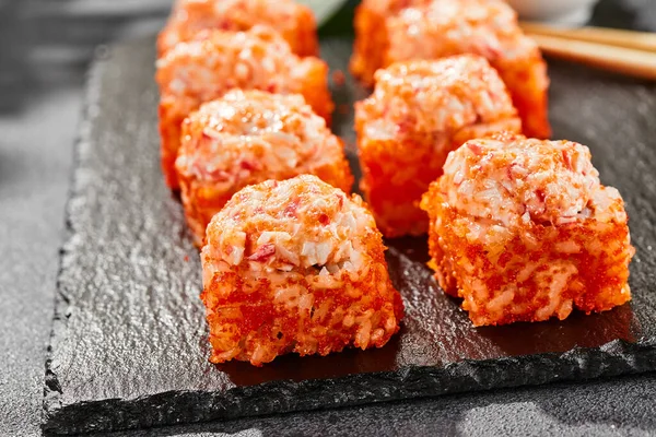 Kara tahtada fırında Maki suşisi. Yengeçli sıcak California maki. Masugo 'lu suşi rulosu, fırında peynir ve yengeç. Siyah arka planı, yaprakları ve sert gölgesi olan Japon tarzı bir menü.