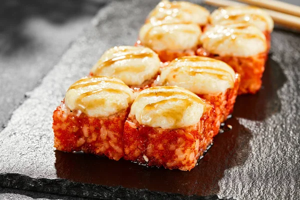 Kara tahtada fırında Maki suşisi. Peynirli sıcak California maki. Dışarıda tobiko soslu, fırında peynirli suşi rulosu. Siyah arka planı, yaprakları ve sert gölgesi olan Japon tarzı bir menü.