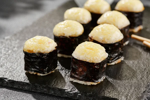 Kara tahtada fırında Maki suşisi. Sıcak peynirli hosomaki rulosu. Peynirli, fırında peynirli sade suşi. Siyah arka planı, yaprakları ve sert gölgesi olan Japon tarzı bir menü.