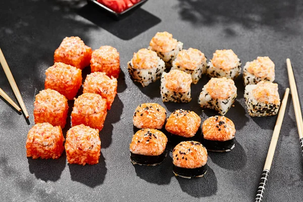 Ateşli maki, kara tahta üzerine kurulmuş. Fırında suşi ve sıcak ekmek. Somon, tobiko ve fırında peynirli suşi. Siyah arka planı, yaprakları ve sert gölgesi olan tarz konsept suşi menüsü