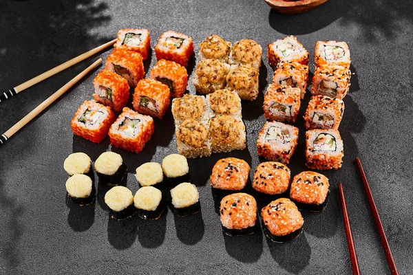 Maki suşisi koyu arkaplanda. Çeşitli ekmeklerle Maki seti. Suşi börekleri ve fırında maki karışımı. Siyah arka planı, yaprakları ve sert gölgesi olan tarz konsept suşi menüsü