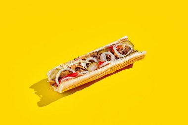 Biftek, soğanlı ve turşulu az pişmiş. Sarı arka planda gölgeli Amerikan fast food 'u. Philadelphia biftekli sandviç moda konsepti. Renk arkaplanındaki abur cubur