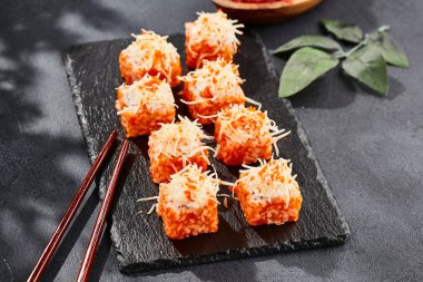 Karanlık taş masada Maki suşisi. Tobiko ile Kaliforniya maki 'si. İçinde balık olan suşi, dışında peynirli maguro. Siyah arka planı, yaprakları ve sert gölgesi olan Japon tarzı bir menü.