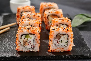 Kara tahtada Maki suşisi. Masaj ve susamlı California maki 'si. Yengeçli suşi, içeride salatalık, dışarıda tobiko. Siyah arka planı, yaprakları ve sert gölgesi olan Japon tarzı bir menü.
