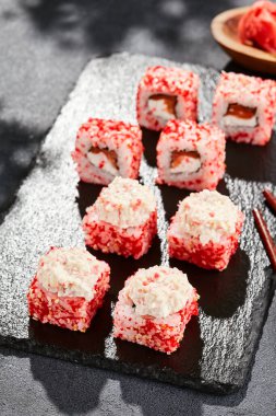 Kara tahtada Maki suşisi. Yengeçli Maki dürümü. Yengeç, krem peynir ve tobika ile suşi rulosu. Siyah arka planı, yaprakları ve sert gölgesi olan Japon tarzı bir menü.