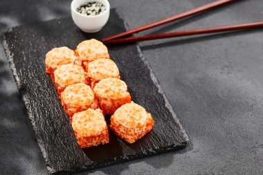 Kara tahtada fırında Maki suşisi. Sıcak California maki ve tobiko. Masaj havyarlı suşi rulosu, fırının üstünde peynir. Siyah arka planı, yaprakları ve sert gölgesi olan Japon tarzı bir menü.