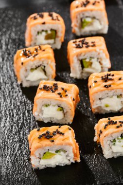 Kara tahtada Maki suşisi. Fırında somonlu sıcak Philadelphia maki. Izgara somon, krem peynir ve avokado ile suşi rulosu. Siyah arka planı, yaprakları ve sert gölgesi olan Japon tarzı bir menü.