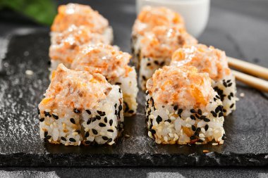 Kara tahtada fırında Maki suşisi. Somon ve peynirli sıcak suşi rulosu. Sushi rulo sushi dışarıda, fırında somon ve peynirli. Siyah arka planı, yaprakları ve sert gölgesi olan Japon tarzı bir menü.