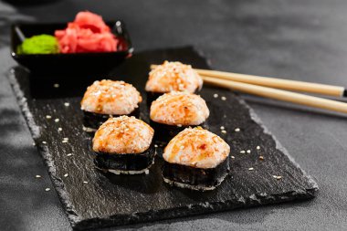 Kara tahtada fırında Maki suşisi. Sıcak unagi maki ve tobiko. Fırında peynirli suşi, masago ve unagi soslu. Siyah arka planı, yaprakları ve sert gölgesi olan Japon tarzı bir menü.