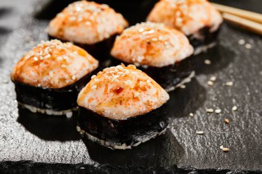 Kara tahtada fırında Maki suşisi. Sıcak unagi maki ve tobiko. Fırında peynirli suşi, masago ve unagi soslu. Siyah arka planı, yaprakları ve sert gölgesi olan Japon tarzı bir menü.