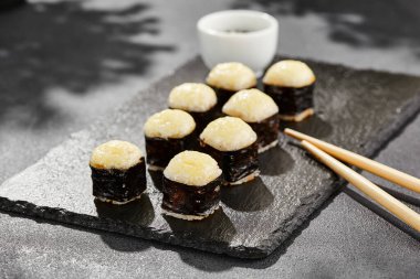 Kara tahtada fırında Maki suşisi. Sıcak peynirli hosomaki rulosu. Peynirli, fırında peynirli sade suşi. Siyah arka planı, yaprakları ve sert gölgesi olan Japon tarzı bir menü.