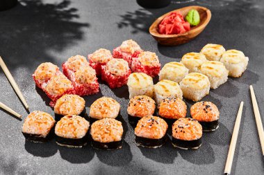 Ateşli maki, kara tahta üzerine kurulmuş. Çeşitli ekmeklerle hazırlanmış fırında suşi. Somon, tobiko, yengeç ve fırında peynirli suşi. Siyah arka planı, yaprakları ve sert gölgesi olan tarz konsept suşi menüsü