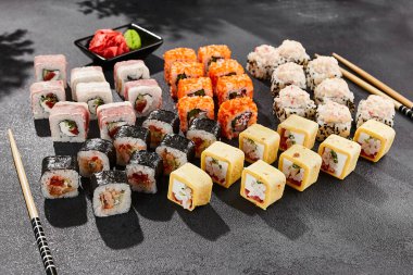 Maki suşisi koyu arkaplanda. Çeşitli rollerle büyük maki seti. Suşi ruloları ve hosomaki 'den kompozisyon. Siyah arka planı, yaprakları ve sert gölgesi olan tarz konsept suşi menüsü