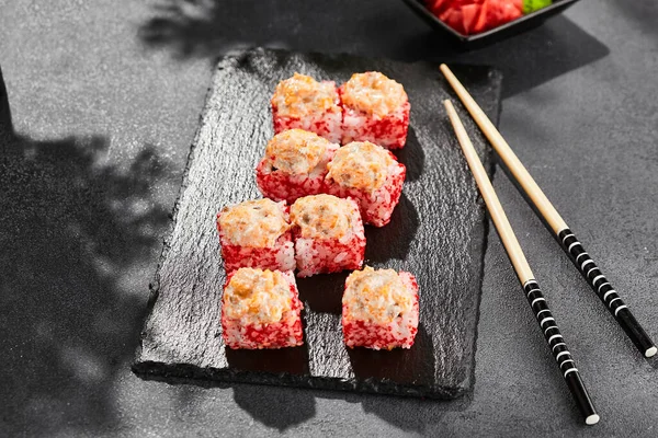 Baked Maki sushi on dark slate. Hot sushi roll with salmon. Sushi roll with tobiko outside, baked fish  and cheese topped. Style concept japanese menu with black background, leaves and hard shadow