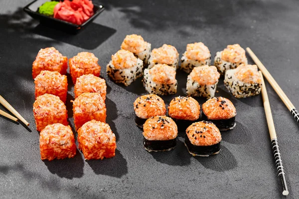 Hot maki set on dark slate. Baked sushi set with hot rolls. Sushi rolls with salmon,tobiko and baked cheese topped. Style concept sushi menu with black background, leaves and hard shadow