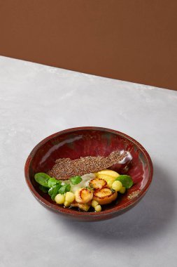 Kereviz ezmeli kızarmış deniz tarağı ve koyu el yapımı seramik tabakta kabak topları. Gri beton arka planda modern servis malzemeleriyle deniz ürünleri tabağı. İlham verici şef.