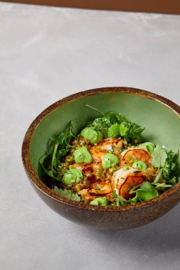 Yeşil kase, karides, kinoa ve el yapımı seramik tabakta avokado kreması. Karanlık modern bulaşık takımında karidesli salata. Modern tarzda sağlıklı yiyecekler..