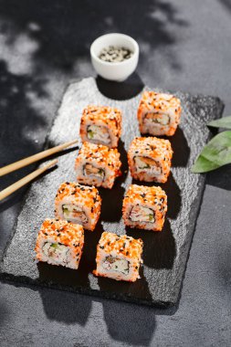Kara tahtada Maki suşisi. Masaj ve susamlı California maki 'si. Yengeçli suşi, içeride salatalık, dışarıda tobiko. Siyah arka planı, yaprakları ve sert gölgesi olan Japon tarzı bir menü.