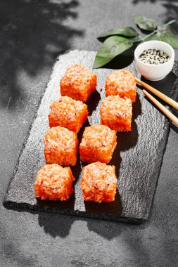 Kara tahtada fırında Maki suşisi. Yengeçli sıcak California maki. Masugo 'lu suşi rulosu, fırında peynir ve yengeç. Siyah arka planı, yaprakları ve sert gölgesi olan Japon tarzı bir menü.