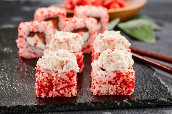 Maki sushi on dark slate.  Maki roll with crab topped. Sushi roll with crab, cream chees and tobika. Style concept japanese menu with black background, leaves and hard shadow