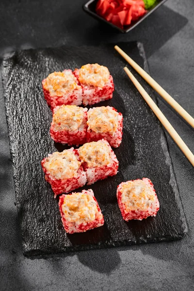 Baked Maki sushi on dark slate. Hot sushi roll with salmon. Sushi roll with tobiko outside, baked fish  and cheese topped. Style concept japanese menu with black background, leaves and hard shadow