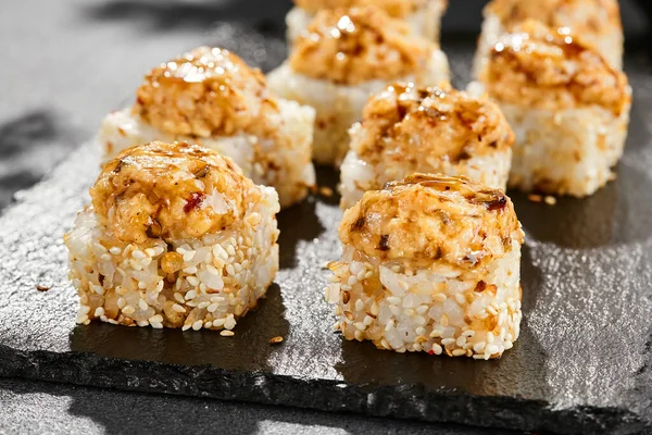 Kara tahtada fırında Maki suşisi. Yılanbalıklı sıcak unagi maki. Fırında yılan balığı, peynir ve unagi soslu suşi rulosu. Siyah arka planı, yaprakları ve sert gölgesi olan Japon tarzı bir menü.