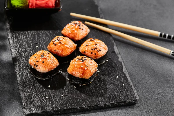 Kara tahtada fırında Maki suşisi. Sıcak unagi maki ve tobiko. Fırında peynirli suşi, masago ve unagi soslu. Siyah arka planı, yaprakları ve sert gölgesi olan Japon tarzı bir menü.